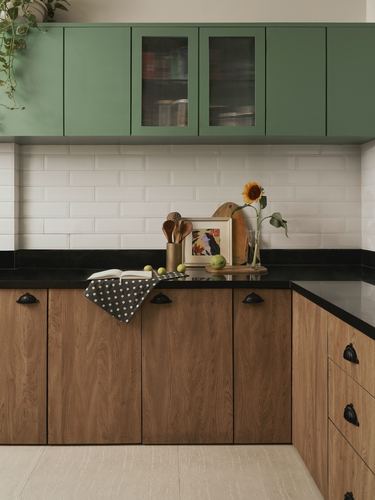 Kitchen corner with sage green upper cabinets, wood lower cabinets, black countertop, and a sunflower on the counter