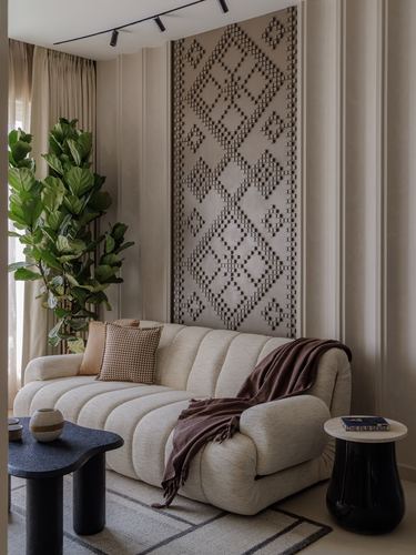 Beige channel-tufted sofa beneath a carved diamond wall panel with a fiddle-leaf plant beside it
