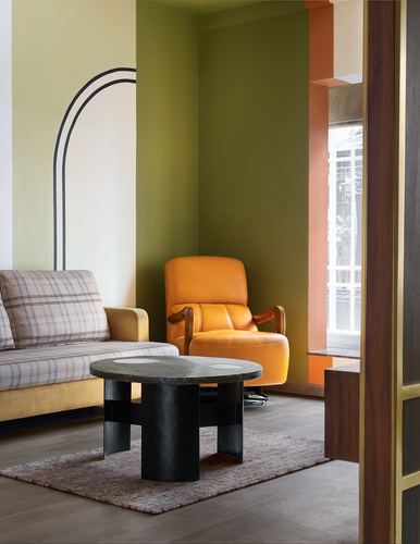 Living room corner with orange leather chair, plaid sofa, and round stone coffee table against olive wall