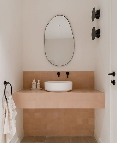 Terracotta zellige tile vanity with white vessel sink and organic-shaped mirror in white bathroom
