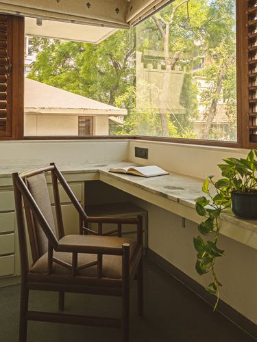 Corner study nook with marble desk, wooden chair, and large window overlooking trees
