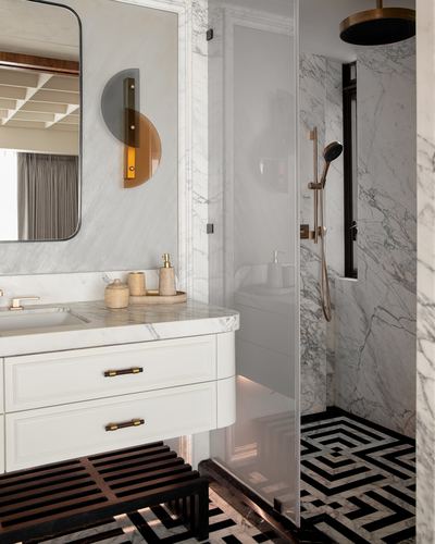 Marble bathroom with brass fixtures, geometric black and white floor tile, and glass shower enclosure