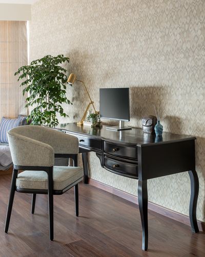 Black curved-leg desk with chair, lamp, monitor and plant against patterned wallpaper