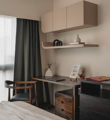 Bedroom study nook with wooden desk, dark drawers, and wall-mounted cabinet