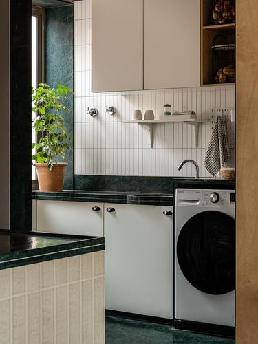 Utility nook with green stone counters, ribbed tile backsplash, and front-load washing machine