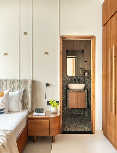 Bedroom with wooden nightstand beside a teak-framed doorway opening to a terrazzo bathroom