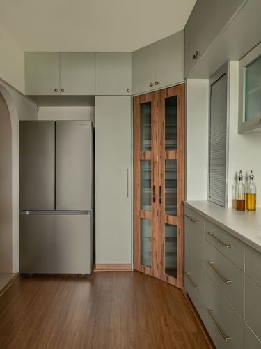 Sage green kitchen with steel fridge, wood-framed fluted glass pantry doors, wood flooring