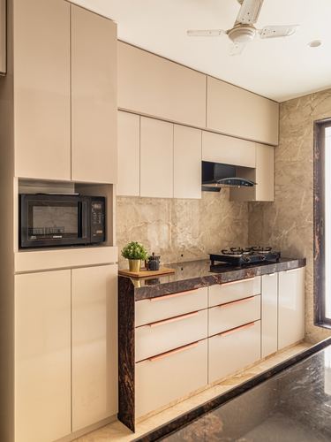 Beige kitchen with stone backsplash, dark countertop, gas hob, and chimney hood in Mumbai apartment