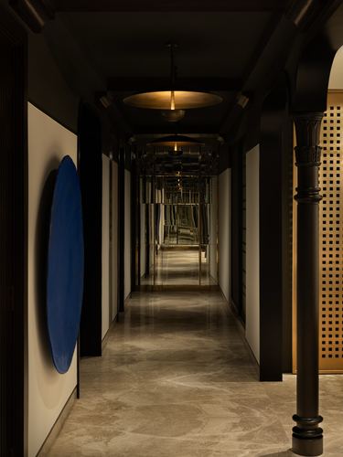Long dark corridor with hanging pendant lights, mirrored ceiling, and a blue circular artwork on the wall