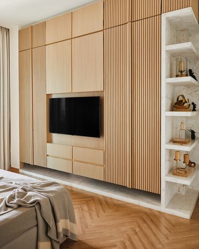 Bedroom with fluted wood wardrobe, built-in tv, and marble open shelving niche beside herringbone floor