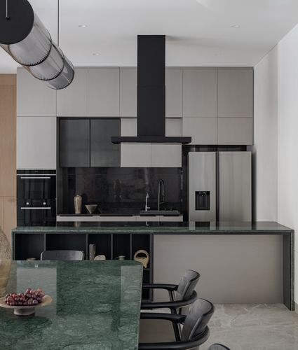 Modern kitchen with green stone island, black hood, grey cabinetry and steel fridge