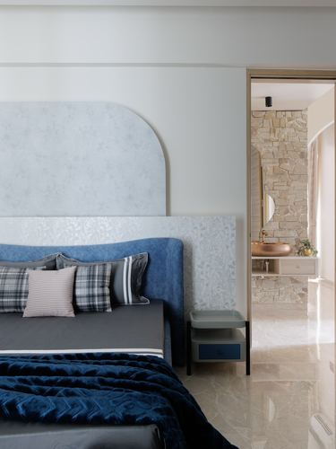 Blue upholstered arched headboard bedroom with view into stone-walled bathroom with copper sink