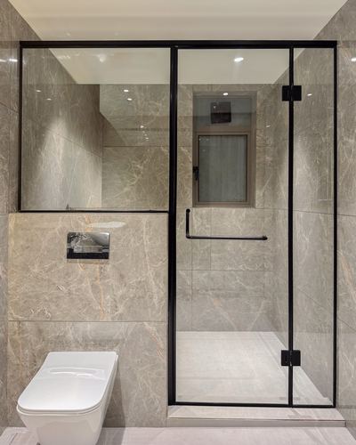 Bathroom with veined stone tile walls, black-framed glass shower enclosure, and wall-hung white toilet