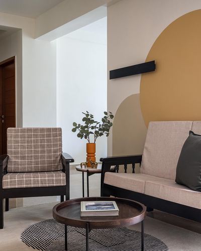 Living room corner with black-framed sofa and armchair against a mustard circle mural, round coffee table with rug.