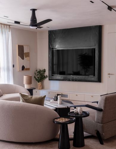 Curved beige boucle sofa faces a dark stone-clad television wall in a fluted-panel living room