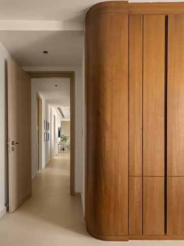 Curved wooden cabinetry wall beside open door leading into a warm-lit corridor