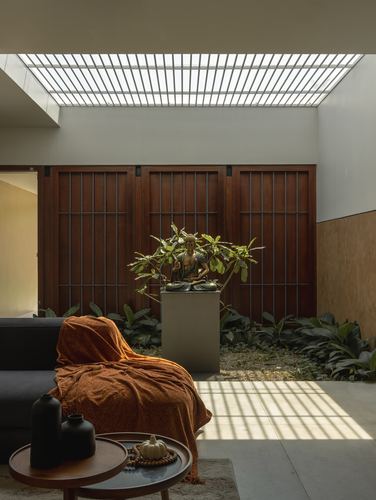 Living room nook facing an interior courtyard with wooden screen wall, buddha statue, and skylight shadows