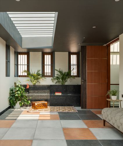 Foyer with skylight, terrazzo bench, barred windows, wooden door, and checkerboard terracotta-grey tile floor.