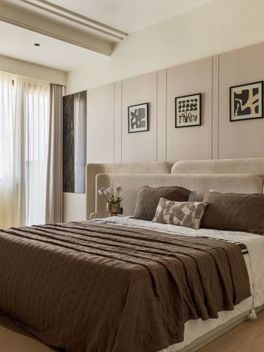 Beige bedroom with upholstered panel headboard, brown linen bedding, and framed abstract art on wall