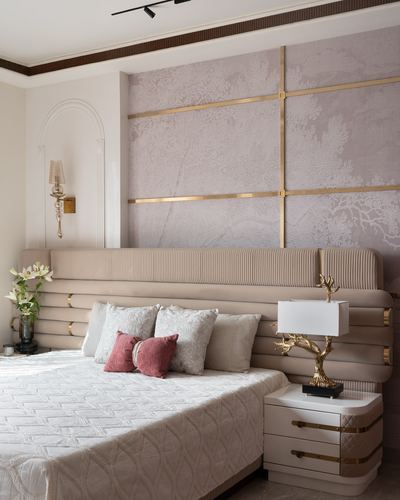 Beige ribbed headboard bed against a blush and gold paneled wall with a brass tree lamp on the nightstand