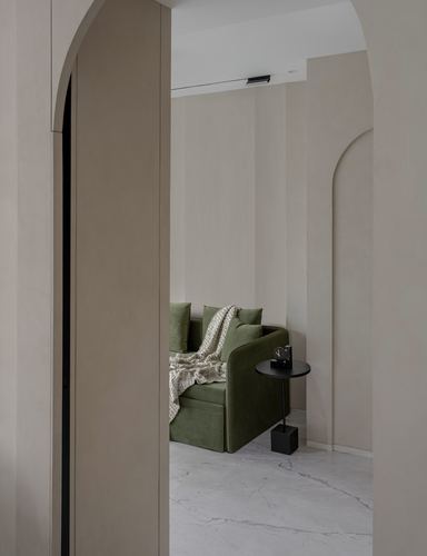 View through arched beige doorways into a living room with an olive green sofa on marble flooring