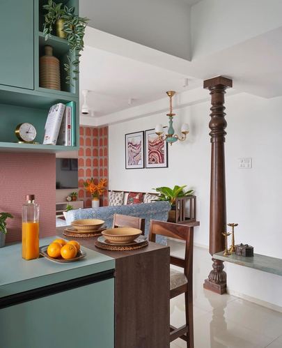 Colorful kitchen counter with fruit and juice, teal cabinetry, and a carved wooden column beyond