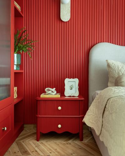 Red fluted nightstand against matching ribbed red wall beside cream upholstered headboard