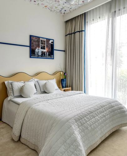 Bedroom with scalloped mustard headboard, blue-trimmed curtains, and framed photograph above bed