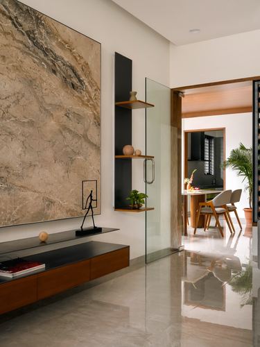Foyer with bookmatched marble wall, floating wood console, and glass door opening to dining area