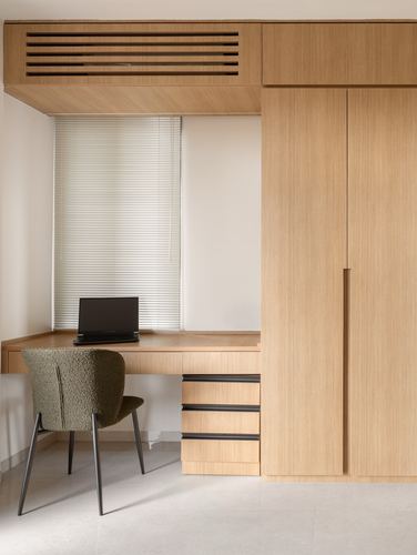 Built-in wood desk with laptop below a window, beside tall wardrobe shutters