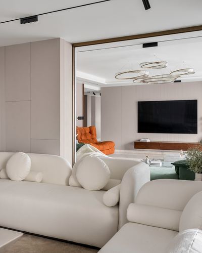 Cream bouclé sofa in foreground opens to living room with orange armchair and ring chandelier