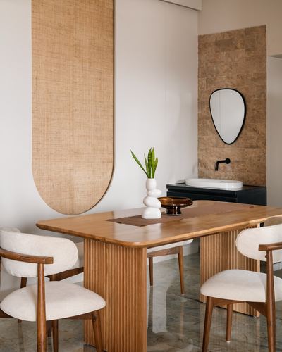 Wooden dining table with fluted base under an arched cane wall panel beside a stone-tiled basin nook