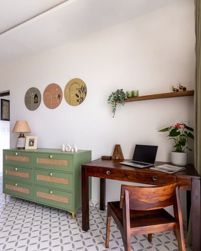 Home study corner with green cane dresser, wooden desk and chair, and circular wall art on patterned tile floor