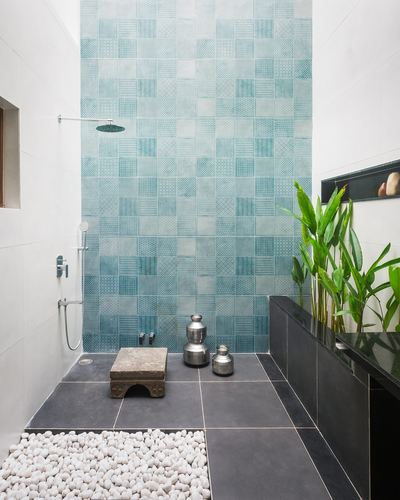 Bathroom shower area with teal patterned tile wall, dark stone floor, and pebble strip.