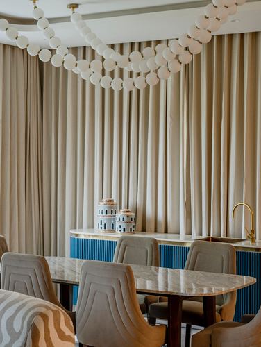 Dining area with marble table, fluted blue console, and cascading bubble chandelier against beige curtains