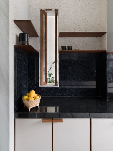 Kitchen corner with dark stone counter, floating wood shelves, and narrow window with plant