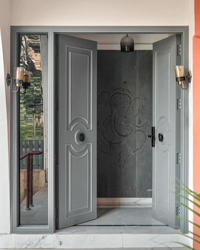 Grey double entrance door open to reveal a Ganesha motif panel, flanked by mirror and sconces