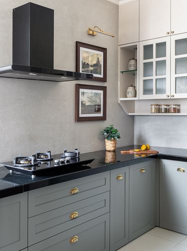 L-shaped kitchen with sage cabinets, black stone counter, black chimney hood, framed art on textured wall