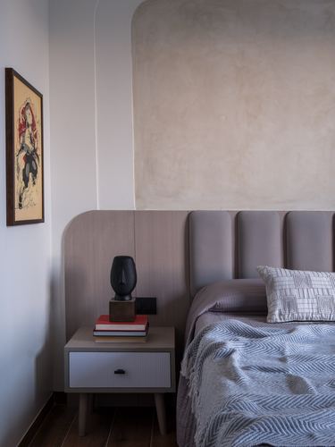 Bedroom corner with arched plaster wall, wood nightstand, and grey tufted headboard