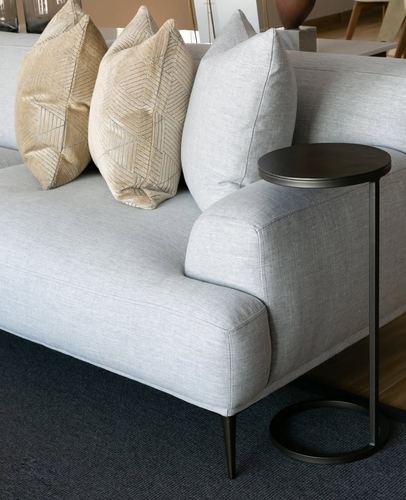 Close-up of grey linen sofa with beige and cream patterned cushions beside a round metal side table