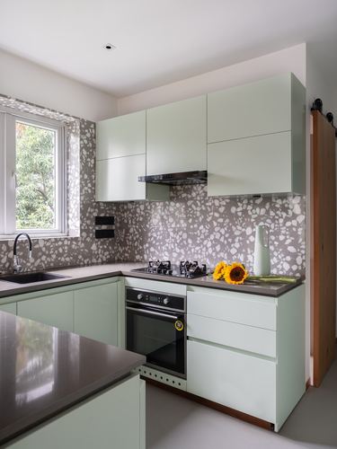 Sage green L-shaped kitchen with terrazzo backsplash, built-in oven, and sunflowers on counter