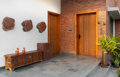 Entry foyer with brick wall, two ribbed wood doors, carved trunk console and wood-slice wall art on grey stone floor