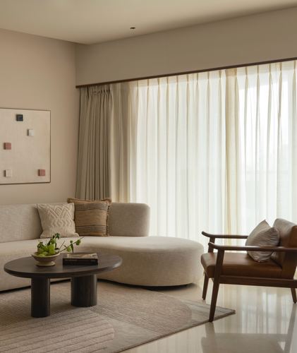 Neutral living room with curved beige sofa, leather armchair, round dark wood coffee table and sheer curtains