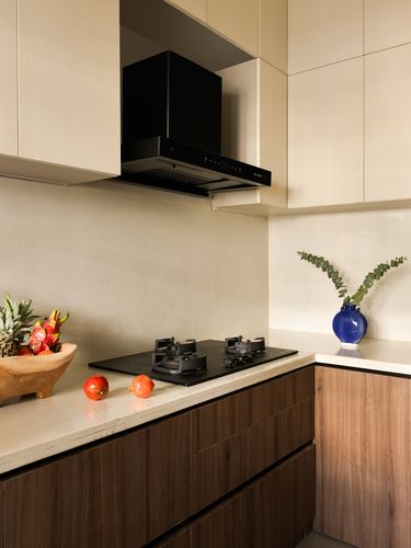 Corner kitchen counter with black chimney hood, gas hob, fruit bowl and blue vase