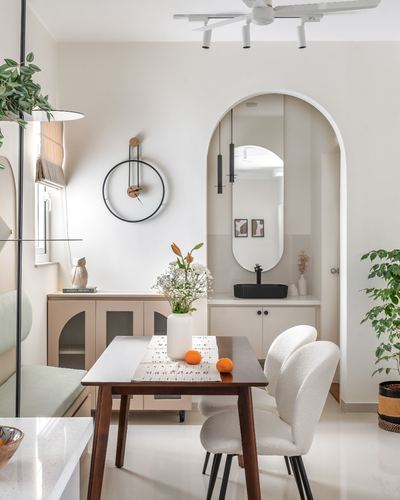 Dining table with boucle chairs beside arched mirrored niche and beige sideboard