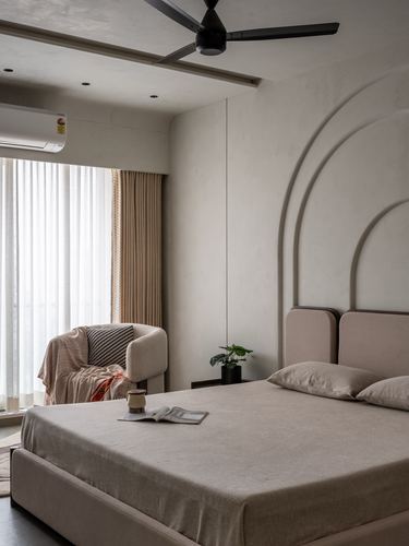Minimalist beige bedroom with arched plaster wall detail behind upholstered headboard and sheer-curtained window