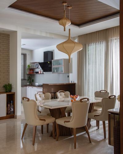 Dining room with marble table, cream tufted chairs, and large teardrop pendant lights under a wood-paneled ceiling.