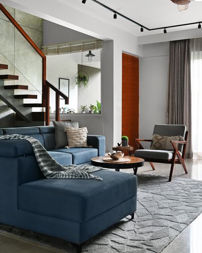 Living room with blue velvet sectional, wooden staircase, and grey patterned rug