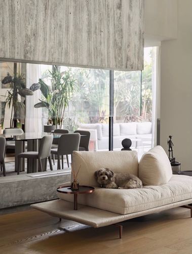 Cream boucle sofa with a small dog beneath a travertine ceiling beam, overlooking a garden