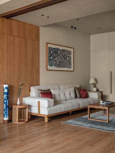 Beige living room with wooden panelling, white tufted sofa, red cushions, and framed artwork.